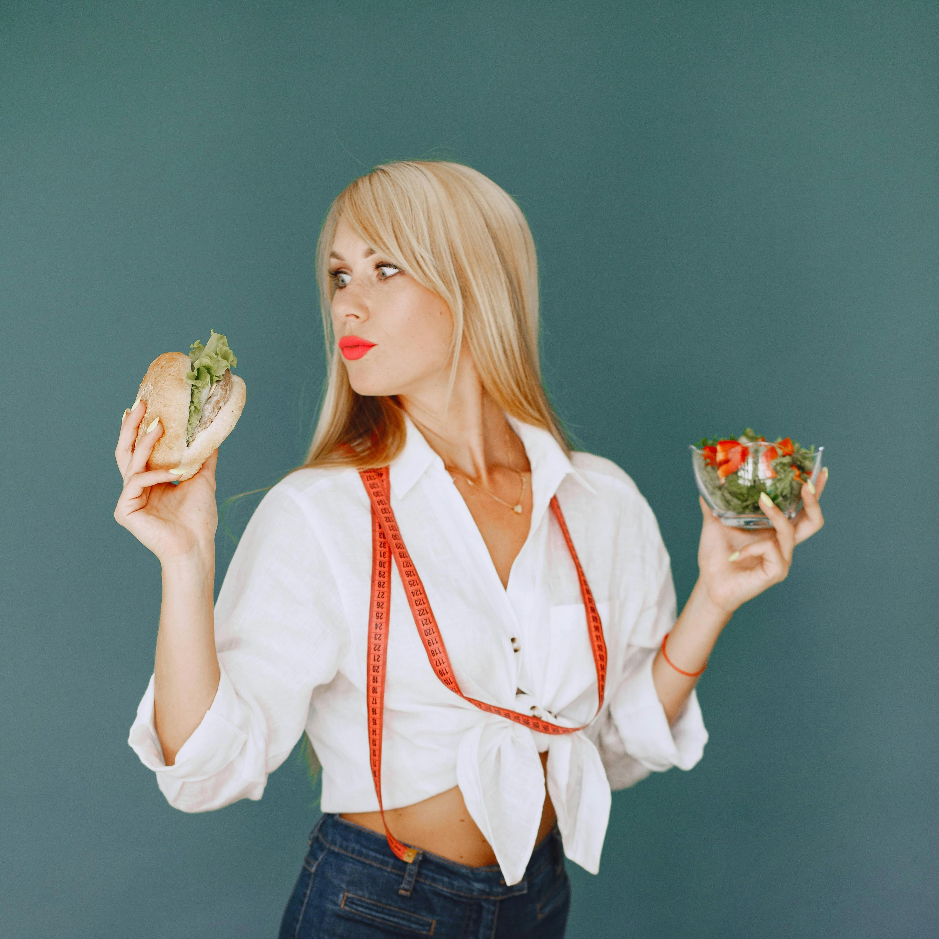 Woman holding a sandwich and salad with vegetables on a table