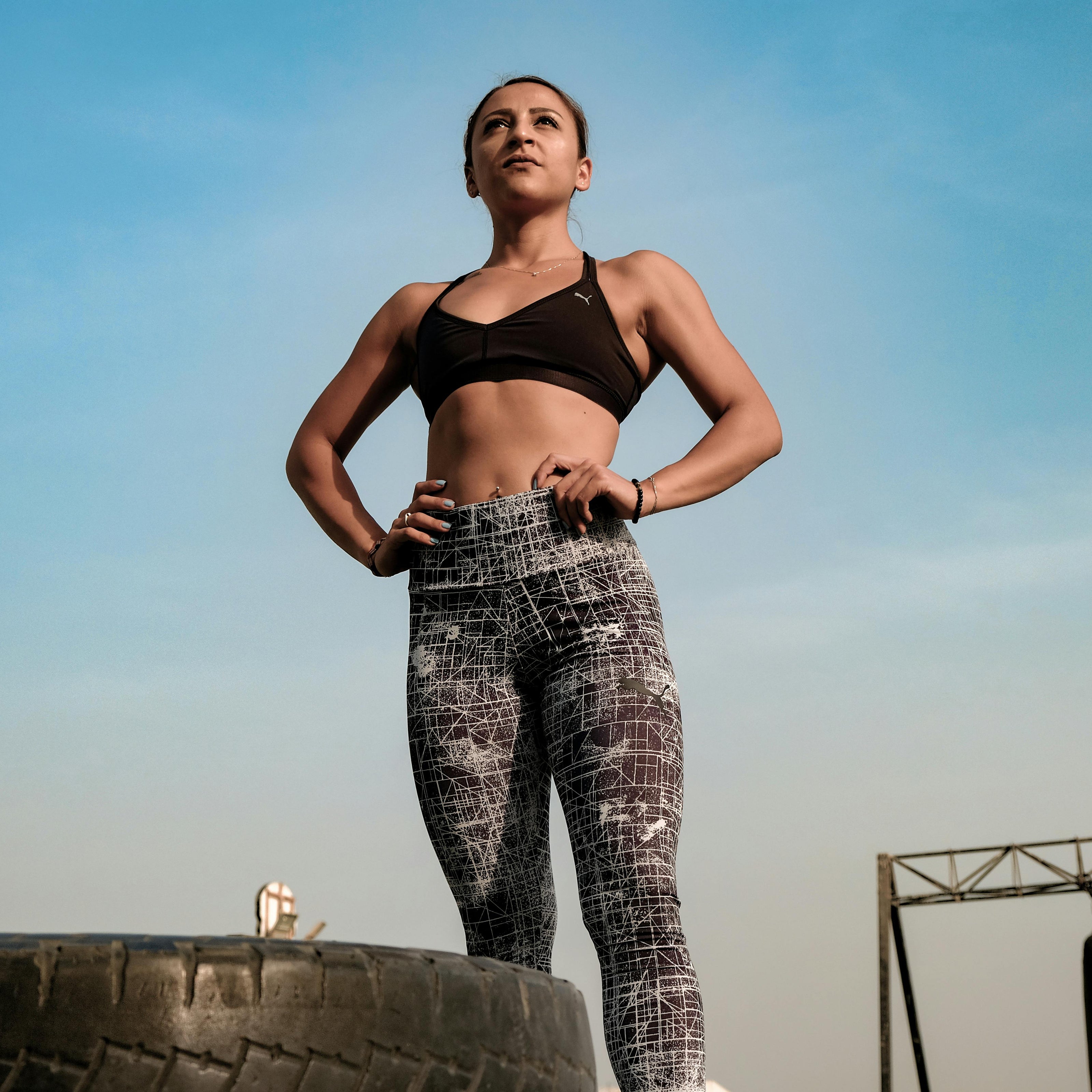 Woman in athletic wear standing on a tire with a clear sky background